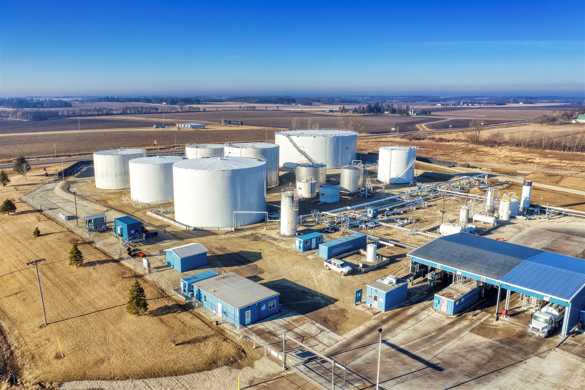 Aerial view of a fuel storage terminal with white tanks, a loading canopy and a tanker truck